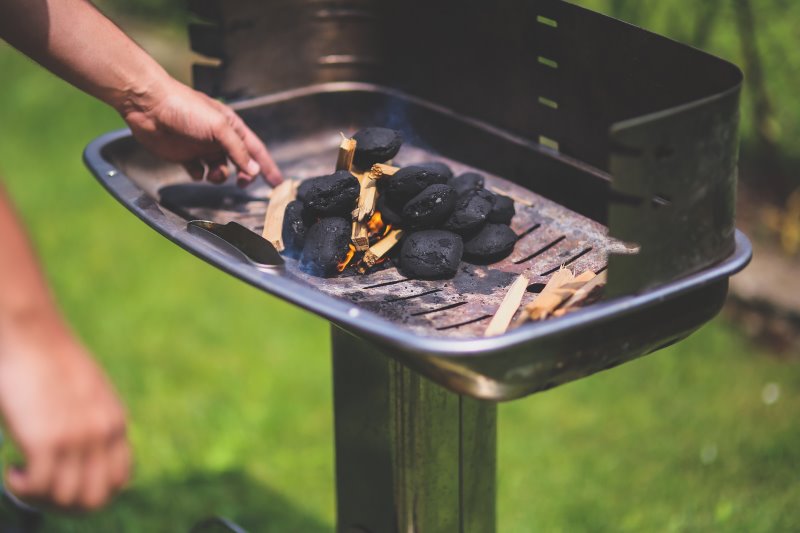 Holzkohle wird auf einen Holzkohlegrill geworfen Holzkohlebriketts veranschaulicht.