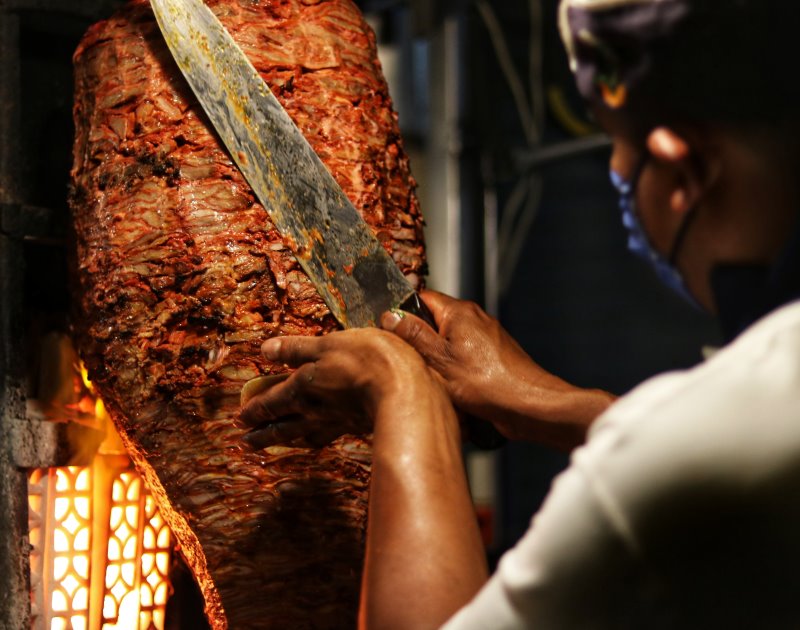Mann schneidet mit scharfem Messer Fleisch von Dönerspieß Döner von Grill mit Messer schneiden