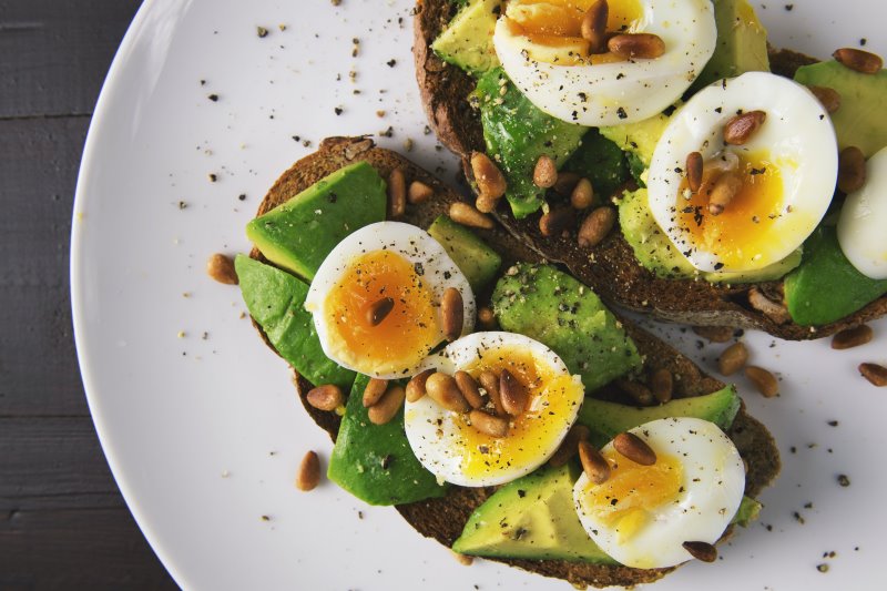 Zwei Brotscheiben, die mit Avocado, Ei und Pinienkernen belegt sind und mit Hilfe von Salz- und Pfeffermühlen gewürzt wurden