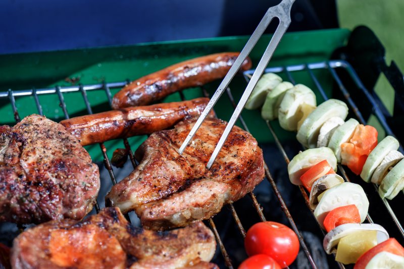 Fleischgabel wendet Fleisch auf einem Grill mit Gemüse Fleischgabel wird beim Grillen verwendet