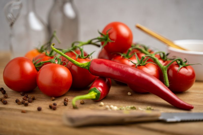Tomaten mit Chili auf Schneidebrett Tomaten und Chilis auf einem Holzbrett mit einem Tomatenmesser.