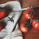 Tomatenmesser liegt neben Tomaten auf einem Holzbrett mit einem Handtuch.