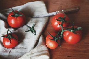 Tomatenmesser liegt neben Tomaten auf einem Holzbrett mit einem Handtuch.