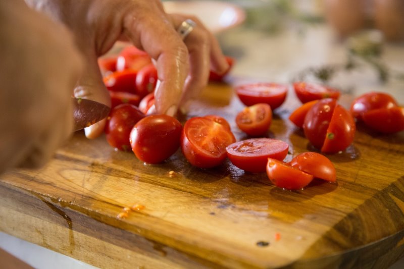 Tomaten werden auf Schneidebrett geschnitten Tomaten werden mit einem Tomatenmesser auf einem Holzbrett halbiert.